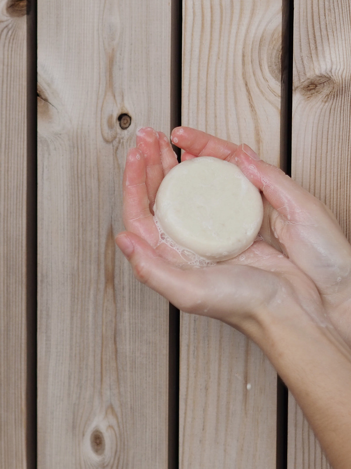 Mellow Mind Balancing sjampobar holdt i hendene med skum, mot lyst treverk