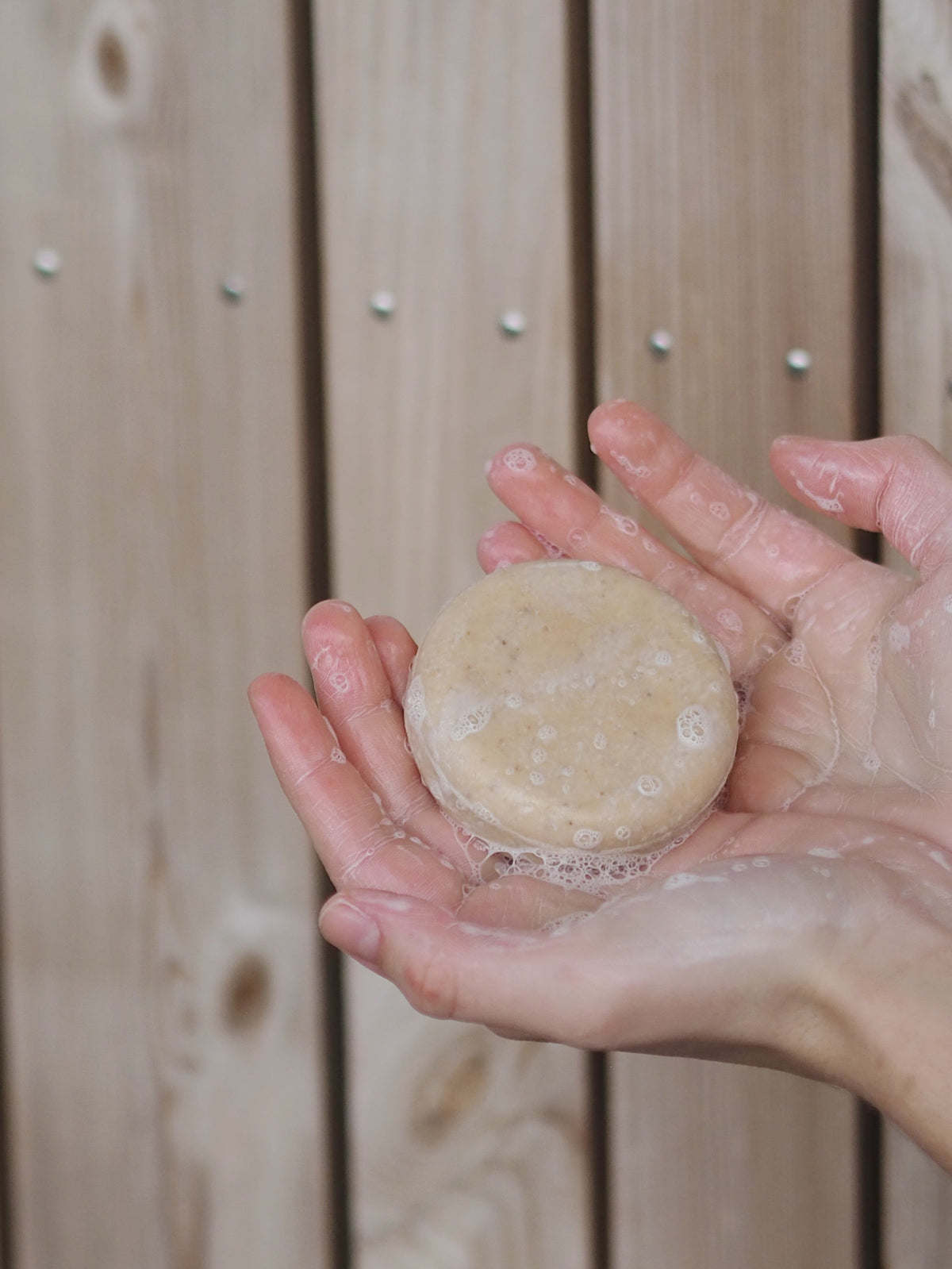 Mellow Mind Hydrating sjampobar holdt i hendene med skum, mot treverk